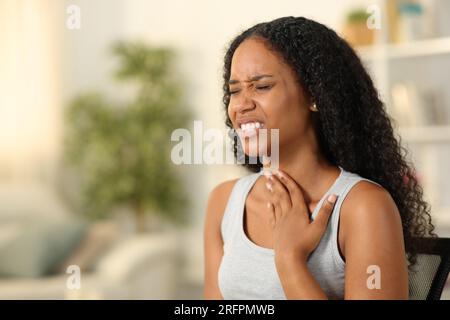 Schwarze Frau, die Halsschmerzen hat und sich zu Hause beschwert Stockfoto