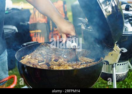 Ein Mann kocht im Sommer Schweinerippchen auf dem Grill im Hof und gießt Soße darüber Stockfoto