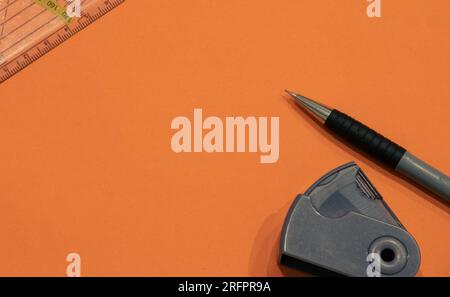 Bleistift, Bleistiftspitzer und ein Geometriegreieck, isoliert auf orangefarbenem Hintergrund mit Kopierraum (auch als leerer Textbereich bezeichnet). Schulhintergrund. Stockfoto