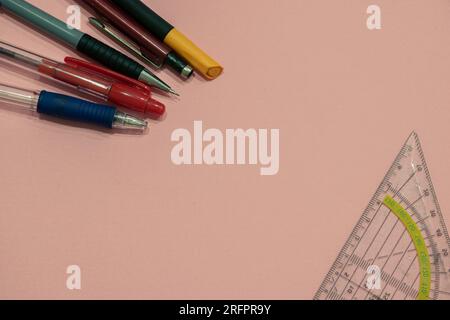Schulzubehör (Stifte und Geometriedreieck), isoliert auf pinkfarbenem Hintergrund mit Kopierraum (auch als leerer Textbereich bezeichnet). Schulhintergrund. Stockfoto