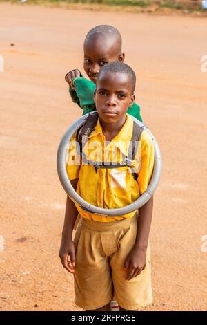 Zwei Kinder posieren, eines trägt eine Lenkradabdeckung um den Hals. Jinja, Uganda. Stockfoto