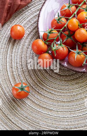 Vertikaler Schuss roter Kirschtomaten auf einer Keramikplatte auf natürlichem Esparto-Hintergrund Stockfoto