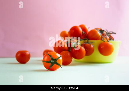Vorderaufnahme roter Kirschtomaten in einer gelben Schüssel auf pastellrosa und grünem Hintergrund. Horizontale Aufnahme. Stockfoto