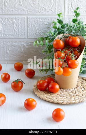 Vorderansicht einer Kartonverpackung mit Kirschtomaten. Null-Kunststoff-Konzept. Weißer Hintergrund und weiße Tabelle. Stockfoto