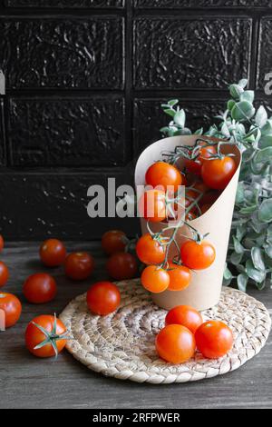 Vorderansicht einer Kartonverpackung mit Kirschtomaten. Null-Kunststoff-Konzept. Schwarzer Hintergrund und grauer Holztisch. Stockfoto