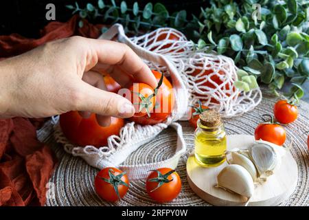 Menschliche Hand hält eine Kirschtomate auf einem Tisch mit gesunden mediterranen Produkten. Horizontale Aufnahme. Stockfoto