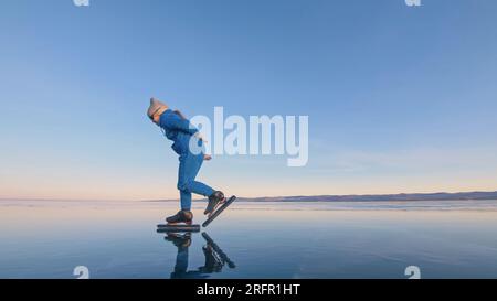 Das Kind trainiert auf Eisschnelllauf. Das Mädchen Schlittschuhe im Winter in Sportbekleidung, Sportbrille, Anzug. Kinder Eisschnelllauf kurze lange Strecke, Kindersport. Zeitlupe im Freien. Stockfoto