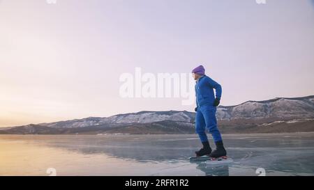 Das Kind trainiert auf Eisschnelllauf. Das Mädchen Schlittschuhe im Winter in Sportbekleidung, Sportbrille, Anzug. Kinder Eisschnelllauf kurze lange Strecke, Kindersport. Zeitlupe im Freien. Stockfoto