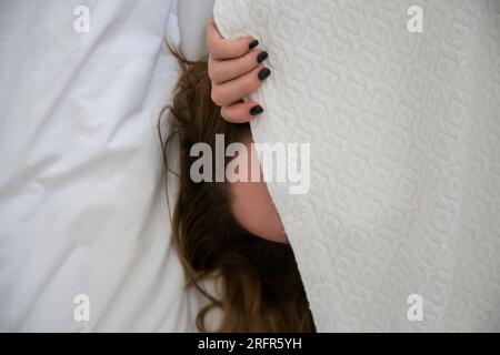 Frau, die sich im Bett unter dem weißen Laken versteckt, bitte noch fünf Minuten. Vorstellung von Depression, Prokrastination oder Faulheit Stockfoto