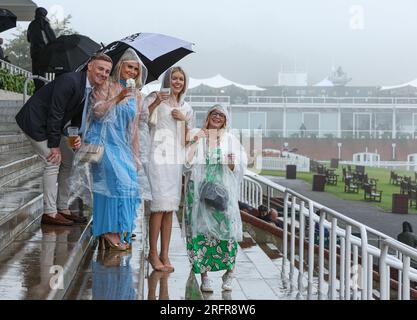 Rennfahrer tragen Ponchos und halten Regenschirme am 5. Tag des Qatar Goodwood Festivals 2023 auf der Rennbahn Goodwood, Chichester. Foto: Samstag, 5. August 2023. Stockfoto