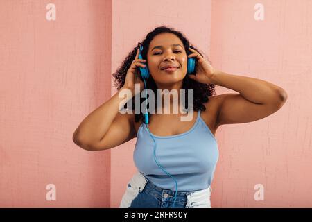 Lächelnde Frau, die Musik hört und blaue Kopfhörer trägt Stockfoto