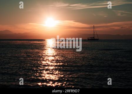 Die Ersten Sonnenstrahlen Beleuchten Die Meeresoberfläche. Silhouette Aus Bergkette Und Yacht. Yachten Werden Mit Aufregenden Abenteuern, Langen Seereisen, In Verbindung Gebracht Stockfoto