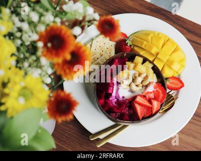Smoothie-Schüssel mit Mango, Erdbeere, Drachenfrucht und Cashew in Kokosnussschale Nahaufnahme Stockfoto