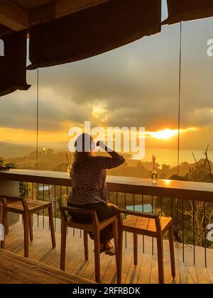 Eine Frau beobachtet den fantastischen Sonnenaufgang in den Bergen von einem Café in der Region Kintamani, Bali Stockfoto
