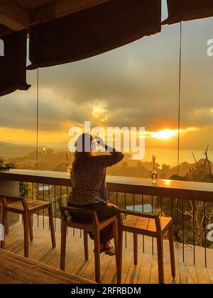 Eine Frau beobachtet den fantastischen Sonnenaufgang in den Bergen von einem Café in der Region Kintamani, Bali Stockfoto