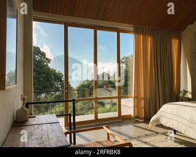 Panoramafenster im Schlafzimmer mit atemberaubendem Blick auf Dschungel und Berge an sonnigen Tagen Stockfoto