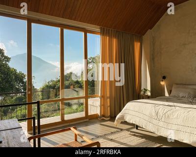 Panoramafenster im Schlafzimmer mit atemberaubendem Blick auf Dschungel und Berge an sonnigen Tagen Stockfoto