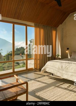 Panoramafenster im Schlafzimmer mit atemberaubendem Blick auf Dschungel und Berge an sonnigen Tagen Stockfoto