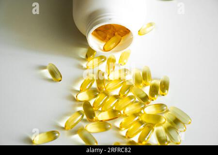 Stapel gelber Softgel-Kapseln Omega-3-Fischöl aus einer weißen Flasche. Dorschleber, Fischöl. Gefüllte weiche Gelzusätze für die Ernährung Stockfoto