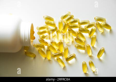 Offene Flasche mit Omega-3-Kapseln. Neben dem Deckel mit Kapseln. Medizinisches Konzept. Haufen gelbe Softgel-Kapseln Omega-3-Fischöl, zerstreut aus A Stockfoto