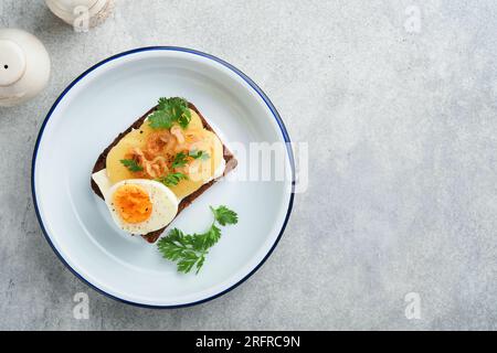 Offenes Sandwich oder Smorrebrod mit Roggenbrot, Hering, Eiern, karamellisierten Zwiebeln, Petersilie und Hüttenkäse auf altem rustikalem Holztischhintergrund. Dani Stockfoto