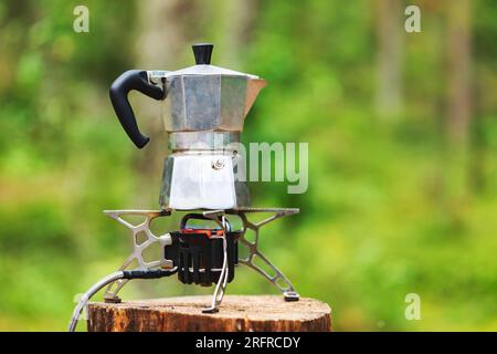 Zubereitung von Kaffee nach italienischem Stil in einer Aluminium-Moka-Kanne auf einem tragbaren Herd während des Campings in einem Wald Stockfoto