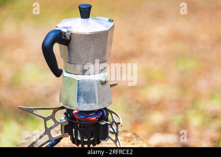 Zubereitung von Kaffee nach italienischem Stil in einer Aluminium-Moka-Kanne auf einem tragbaren Herd während des Campings in einem Wald Stockfoto