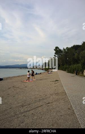 Panoramablick neben einem Seeufer, umgeben von einem Park bei bewölktem Sonnenuntergang Stockfoto