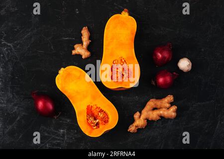 Roher Butternusskürbis mit roten Zwiebeln, Ingwer und Knoblauch auf schwarzem Hintergrund. Zutaten für Kürbissuppe. Draufsicht, flach liegend. Stockfoto