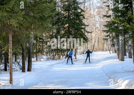 Zwei Skifahrer laufen auf einer Skipiste in einem Winterwald mit Schneetreiben unter der hellen Sonne Stockfoto