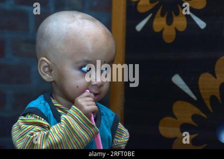 18 Monate altes süßes kahles Baby putzt Zähne mit Zahnbürste, Backsteinwand Hintergrund Stockfoto
