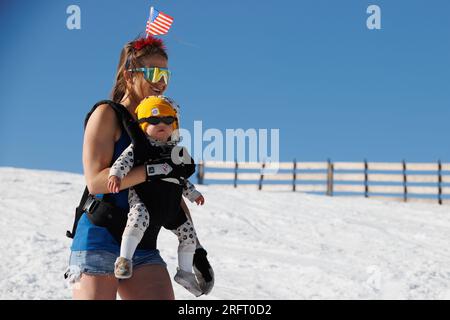 Mammoth Lakes, Kalifornien. 4. Juli 2023. Eine Frau fährt mit einem Baby und einer amerikanischen Flagge auf dem Kopf im Mammoth Mountain Ski Resort an einem klaren Sommertag. Stockfoto
