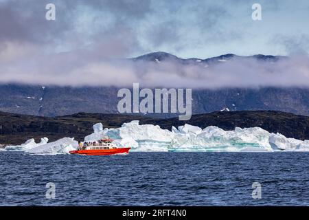 Touristenboot inmitten von Eisbergen und Bergen in der Nähe von Rodebay, Grönland Stockfoto