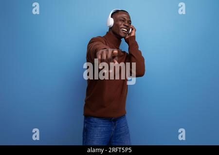 Ein attraktiver, energiegeladener junger afrikanischer Mann, der Musik mit Kopfhörern im Hintergrund mit Kopierbereich hört Stockfoto