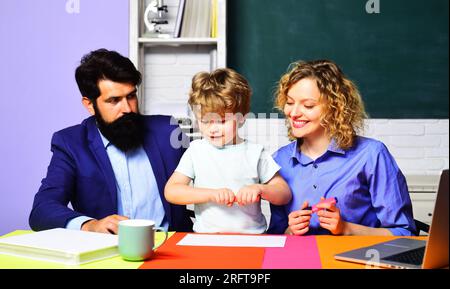 Kind aus der Grundschule mit Eltern in der Schule. Lehrer, die Kindern aus der Grundschule bei Hausaufgaben helfen. Schüler mit Eltern im Klassenzimmer Stockfoto