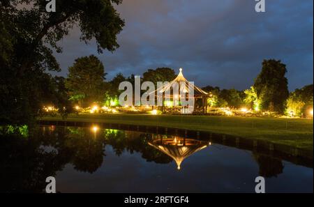 Augsburg, Deutschland. 05. Aug. 2023. Während der Lichterzauber stehen die Lichter im Botanischen Garten neben dem beleuchteten Rosenpavillon, der sich in einem Teich spiegelt. Jeden Samstag, bis zum 13. August, gehen im Botanischen Garten unzählige Lichter in der Dämmerung an. Zu diesem Zweck ist der Botanische Garten bis Mitternacht geöffnet. Kredit: Stefan Puchner/dpa/Alamy Live News Stockfoto