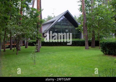 Blick auf ein Restaurant im Wald. Wunderschönes Gebäude mit Panoramafenstern. Vor den Fenstern - Kiefern und Rasen. Der Schaden am Gebäude Stockfoto