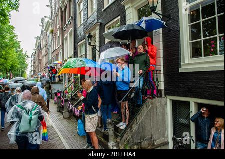 Amsterdam, Niederlande. 05. Aug. 2023. Während der Veranstaltung sehen die Leute die Parade unter ihrem Schirm. Die Kanalparade beginnt gegen Mittag und dauert den ganzen Nachmittag. Rund 80 Schiffe verschiedener Organisationen und gemeinnützige Organisationen nehmen an der Veranstaltung Teil. Für die Grachtenparade ist Amsterdam Gay Pride berühmt. Es ist die Krönung ihres zweiwöchigen Festivals, das mehr als 200 Veranstaltungen umfasst. Die Boote starten am Scheepvaart-Museum im östlichen Teil des Stadtzentrums und fahren in Richtung Amstel. Kredit: SOPA Images Limited/Alamy Live News Stockfoto