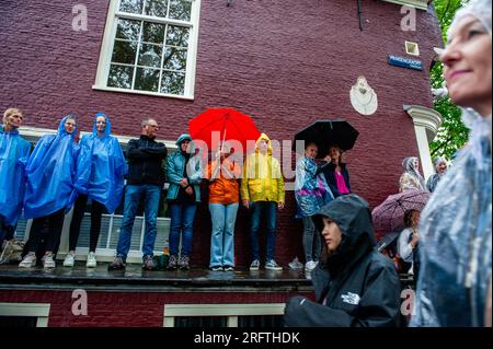 Amsterdam, Niederlande. 05. Aug. 2023. Man sieht, wie sich die Menschen während des Ereignisses von den starken Regenfällen abdecken. Die Kanalparade beginnt gegen Mittag und dauert den ganzen Nachmittag. Rund 80 Schiffe verschiedener Organisationen und gemeinnützige Organisationen nehmen an der Veranstaltung Teil. Für die Grachtenparade ist Amsterdam Gay Pride berühmt. Es ist die Krönung ihres zweiwöchigen Festivals, das mehr als 200 Veranstaltungen umfasst. Die Boote starten am Scheepvaart-Museum im östlichen Teil des Stadtzentrums und fahren in Richtung Amstel. Kredit: SOPA Images Limited/Alamy Live News Stockfoto