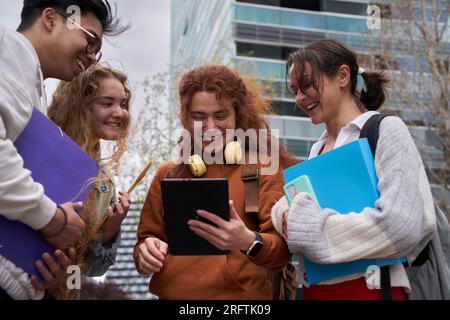 Gruppe von Schülern, die sich ein digitales Tablet teilen, um das Internet außerhalb des Campus zu überprüfen Stockfoto