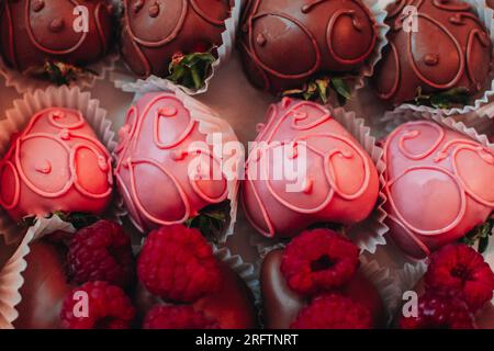 Rosafarbene, mit Schokolade überzogene Erdbeeren mit frischen Himbeeren. Süßigkeiten-Sammlung. Schmackhaftes Urlaubsset. Draufsicht Stockfoto