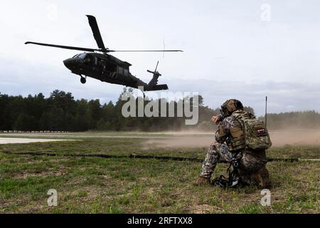 Ein Loading Zone Controller mit der lettischen Nationalarmee beobachtet einen UH-60 Black Hawk, der sich während des 2023. NATO Best Sniper Competition in Camp Adazi, Lettland, am 1. August einer Landezone nähert. Die Teams standen Wind, Regen, Bewegung und eingeschränkter Sicht gegenüber, als sie aus einer Höhe von etwa 50 Metern und einer Entfernung von 200 Metern auf fünf Ziele schossen. Der Wettbewerb, der von Helikopterteams der Task Force Knighthawk, 3. Combat Aviation Brigade, unterstützt 4. Infanterie Division, unterstützt wurde, bestand aus dreiköpfigen Teams, die 12 NATO-Verbündete vertreten: Bulgarien, Kanada, Kroatien Stockfoto