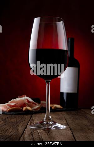 Werbespot Glas, Flasche Rotwein mit leerem Etikett und Jamon serrano auf rostigem braunem Hintergrund. Modell, Vorderansicht Stockfoto