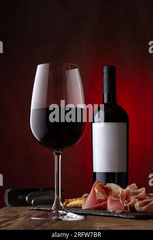 Werbespot Glas, Flasche Rotwein mit leerem Etikett und Jamon serrano auf rostigem braunem Hintergrund. Modell, Vorderansicht Stockfoto