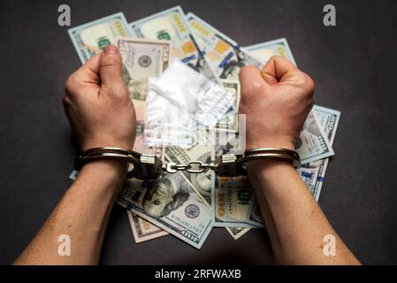 Mann in Handschellen mit Geld und Drogen auf dunklem Hintergrund. Stockfoto