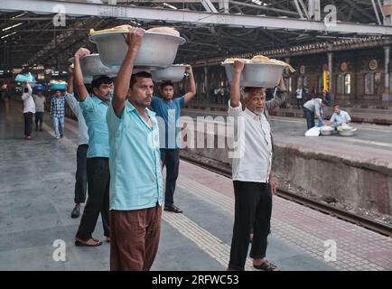 Gepäckträger am Chhatrapati Shivaji Maharaj Terminus in Mumbai, Indien, die Waren auf ihren Köpfen trugen und auf einen lokalen Zug warteten, der sie transportierte Stockfoto