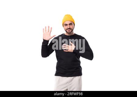 Ein junges, brutales männliches Model in einer schwarzen Jacke und einer gelben Mütze sieht vor der Kamera freundlich aus Stockfoto