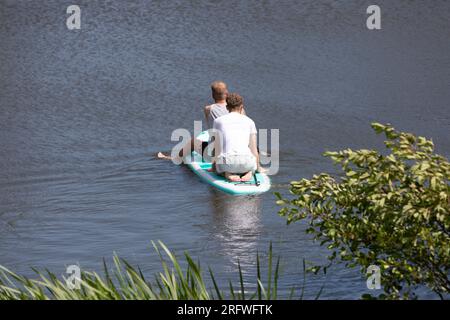 Zwei junge Männer auf einem Paddelbrett auf einem ruhigen Kanal Stockfoto