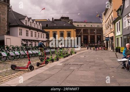 Mann und Frau, die ein OBOS E-Bike vom Abholort auf dem gepflasterten Platz im alten Bergen Norwegen Europa fahren Stockfoto