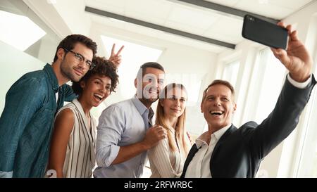 Glückliche Momente. Eine Gruppe lächelnder Kollegen, die Selfies machen und Gesten machen, während sie im modernen Büro stehen Stockfoto